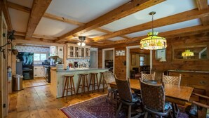 Una cocina rústica con vigas de madera, una isla central con taburetes y un comedor con candelabro.