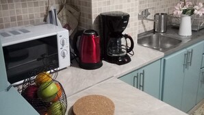 A kitchen with a microwave, coffee maker, and kettle on the counter. There is a fruit basket and a cork board on the countertop. - Mets Near From Panathenaic Kallimarmaro Stadium (Athens)