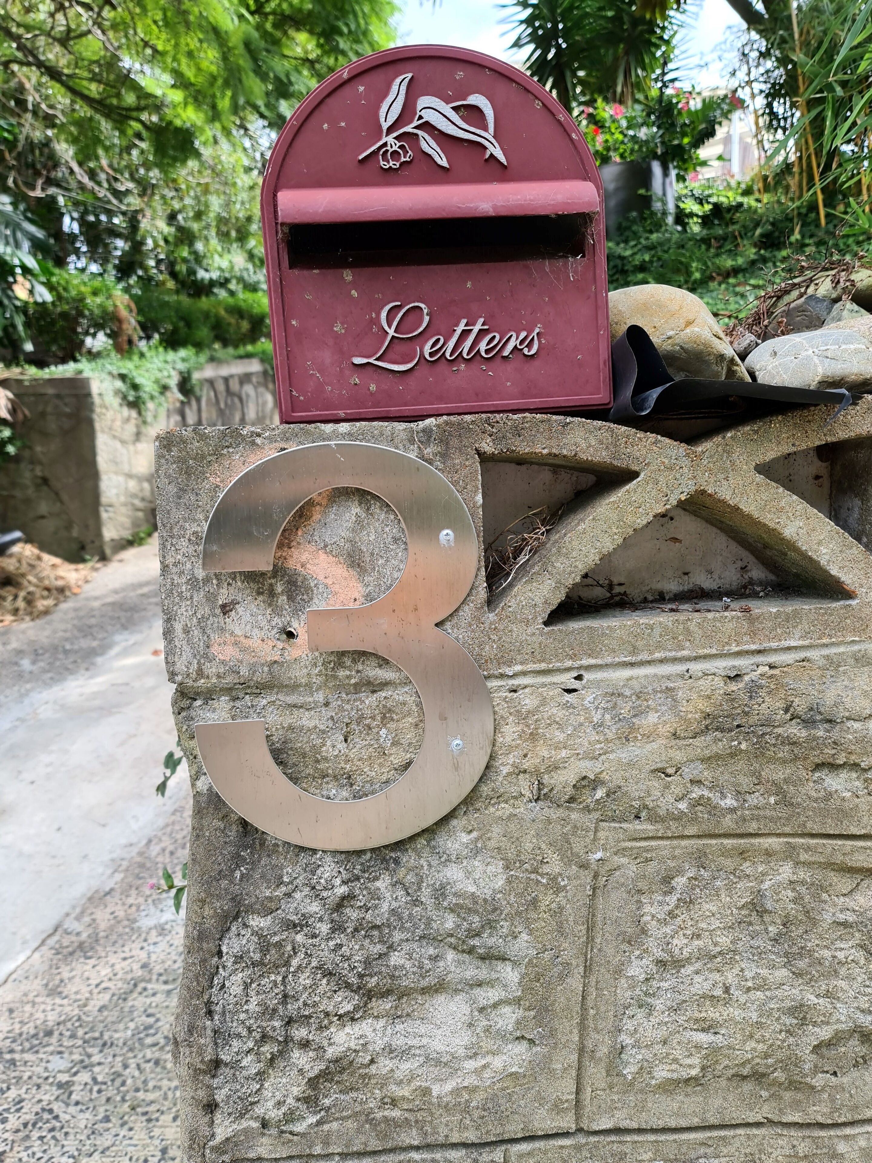 Une boîte aux lettres portant l’inscription « Courrier », fixée à un mur de pierre sur lequel est apposé un grand panneau avec le chiffre « 3 ».