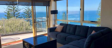 A modern living room with a large window overlooking a coastal view, a dark-colored sofa, and a small coffee table.
