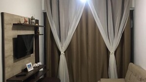 Ett vardagsrum med en soffa, en tv som är monterad på en träpanel, ett litet bord med ett fotoram och en taklampa.