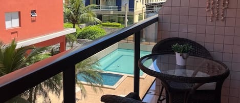A balcony with a view of a swimming pool, a red building, and a multi-story complex.