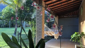 A covered patio area with a hammock, potted plants, and a brick wall. - Guaeca, the paradise of the North Coast. (São Paulo)
