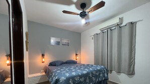 A bedroom with a bed, ceiling fan, wall-mounted lights, and a window with curtains. - Guaeca, the paradise of the North Coast. (São Paulo)