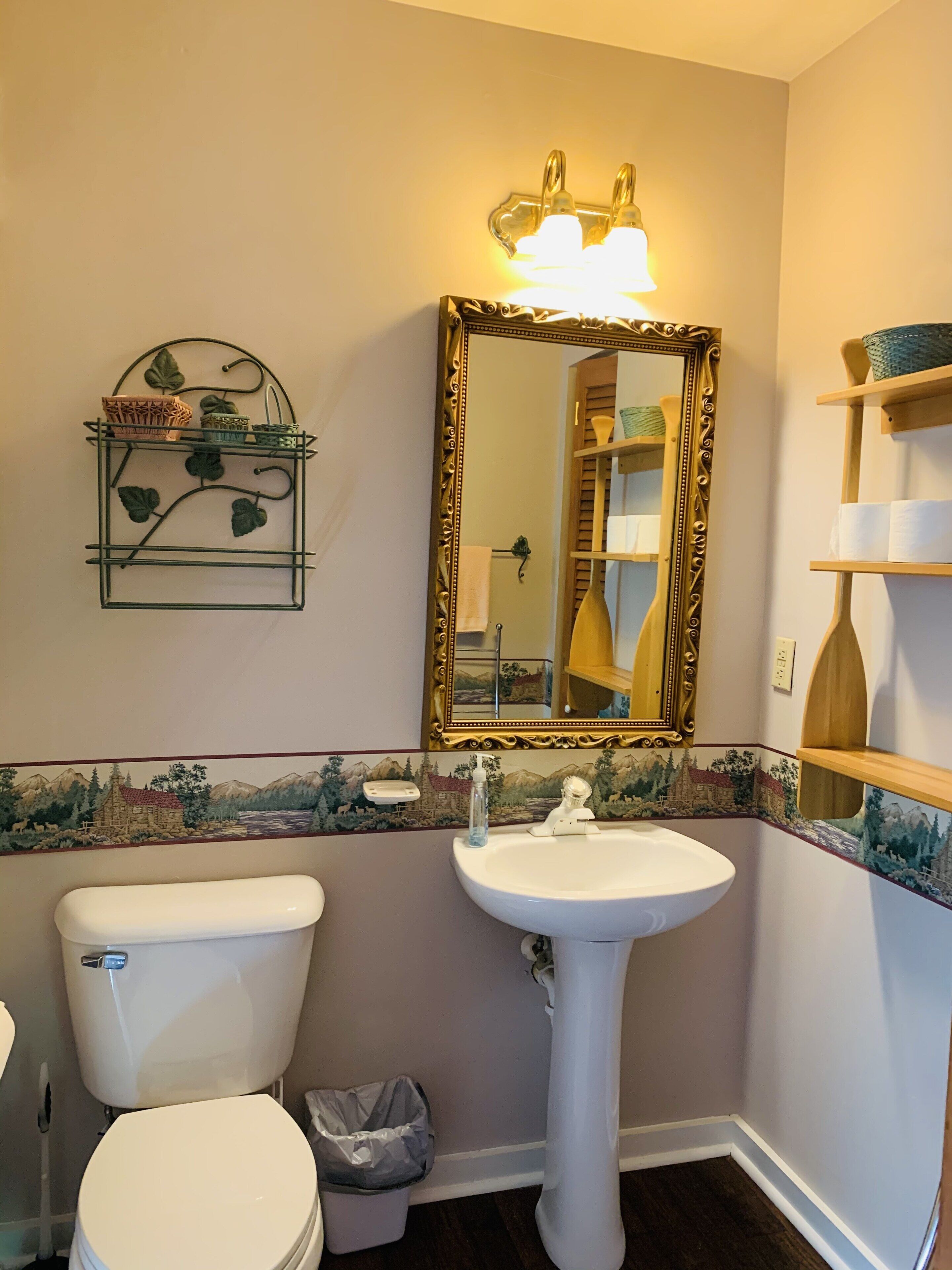 Ein Badezimmer mit Toilette, Waschbecken und Spiegel. Eine dekorative Ablagefläche mit Körben und einem Mülleimer.