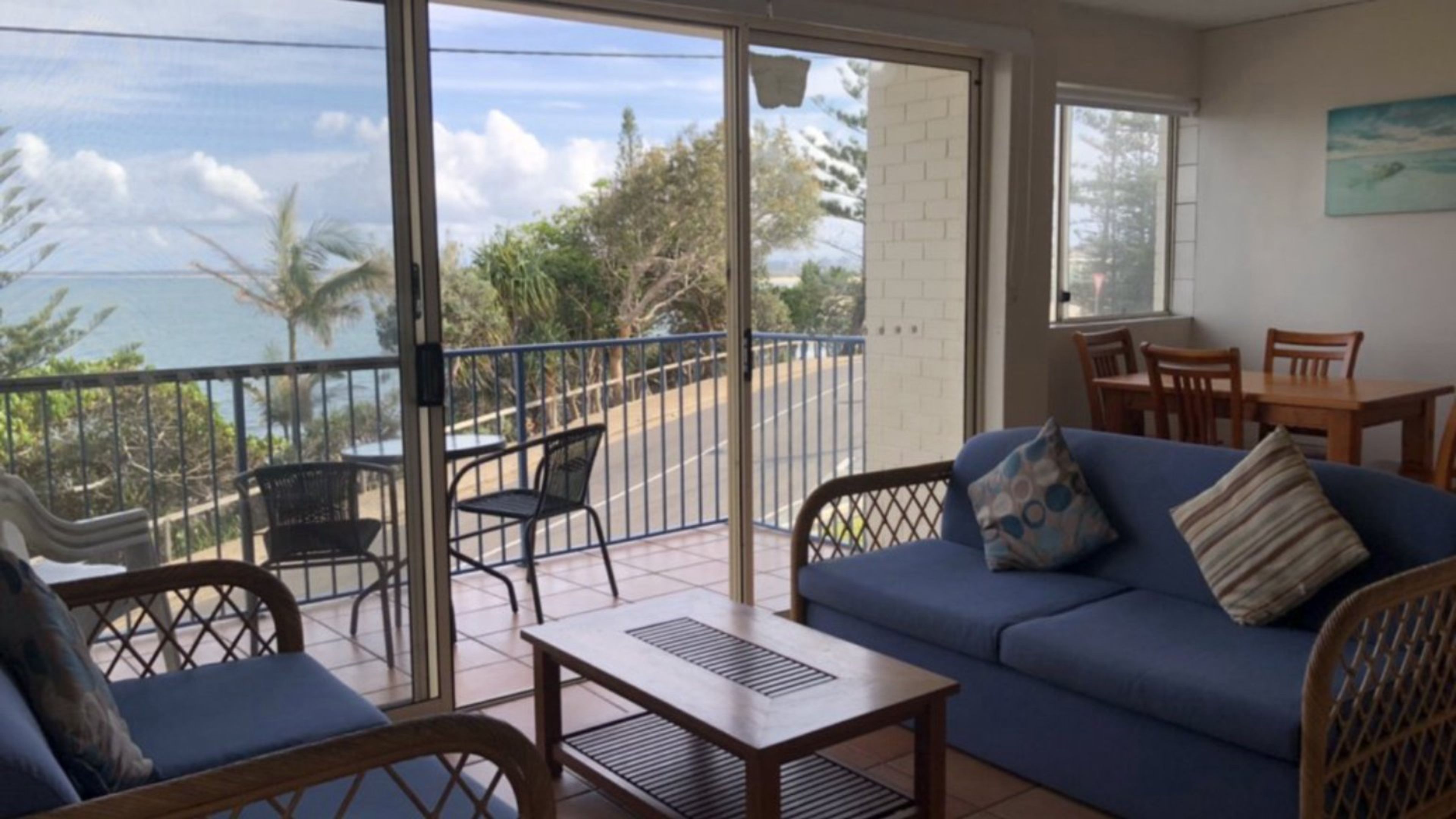 Un balcon avec vue sur l’océan, un canapé bleu et une table à manger avec des chaises.