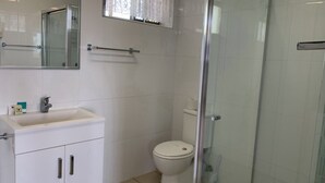 A bathroom with a white sink, mirror, toilet, and glass shower enclosure.