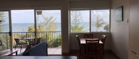A room with a balcony, a dining table with chairs, and a view of the ocean.