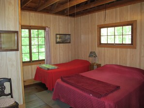 Una habitación con paneles de madera, dos camas, una silla, una lámpara y un cuadro en la pared.