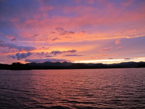 Un atardecer sobre un lago tranquilo con montañas al fondo.