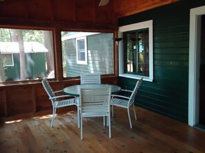 Una cabaña de madera con una mesa redonda y cuatro sillas, ventanas amplias y vista a otra cabaña.