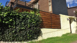 A modern house with a wooden balcony, a large hedge, and a clear blue sky. - Yemanya Hostal (Concon)