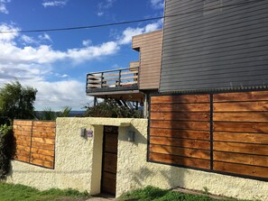 A modern building with a wooden deck, a textured wall, and a wooden gate. - Yemanya Hostal (Concon)