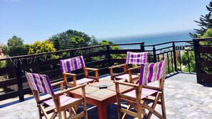 A wooden deck with four chairs and a table, overlooking a scenic view of the ocean. - Yemanya Hostal (Concon)