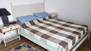 Un lit bien fait, recouvert d’une couvre-lit à carreaux, avec deux oreillers, une table de chevet dotée d’une lampe et une petite étagère.