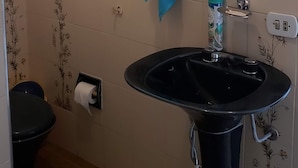 Une salle de bain avec un lavabo noir, un miroir, un porte-serviettes, des toilettes et une fenêtre donnant sur l’extérieur.