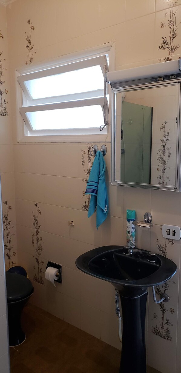 A bathroom with a black sink, a mirror, a towel rack, a toilet, and a window with a view of the outside. - Apartamento Enseada - Ed. Mabe (Balneario Guarujá)