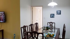 Un coin repas avec une table en verre, des chaises en bois, un luminaire au plafond et un téléviseur fixé au mur.