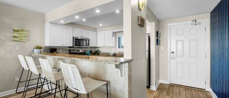 A modern kitchen with white cabinets, a granite countertop, and a built-in island with bar stools.