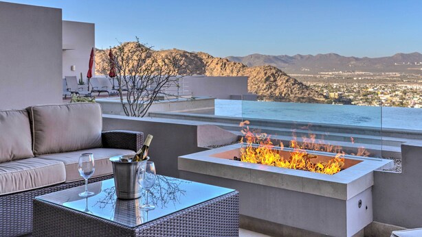 A rooftop terrace with a fire feature, outdoor seating, and a view of a city and mountains.