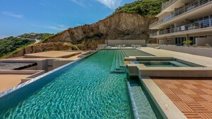 A pool area with clear water, a wooden deck, and a view of a cliff.