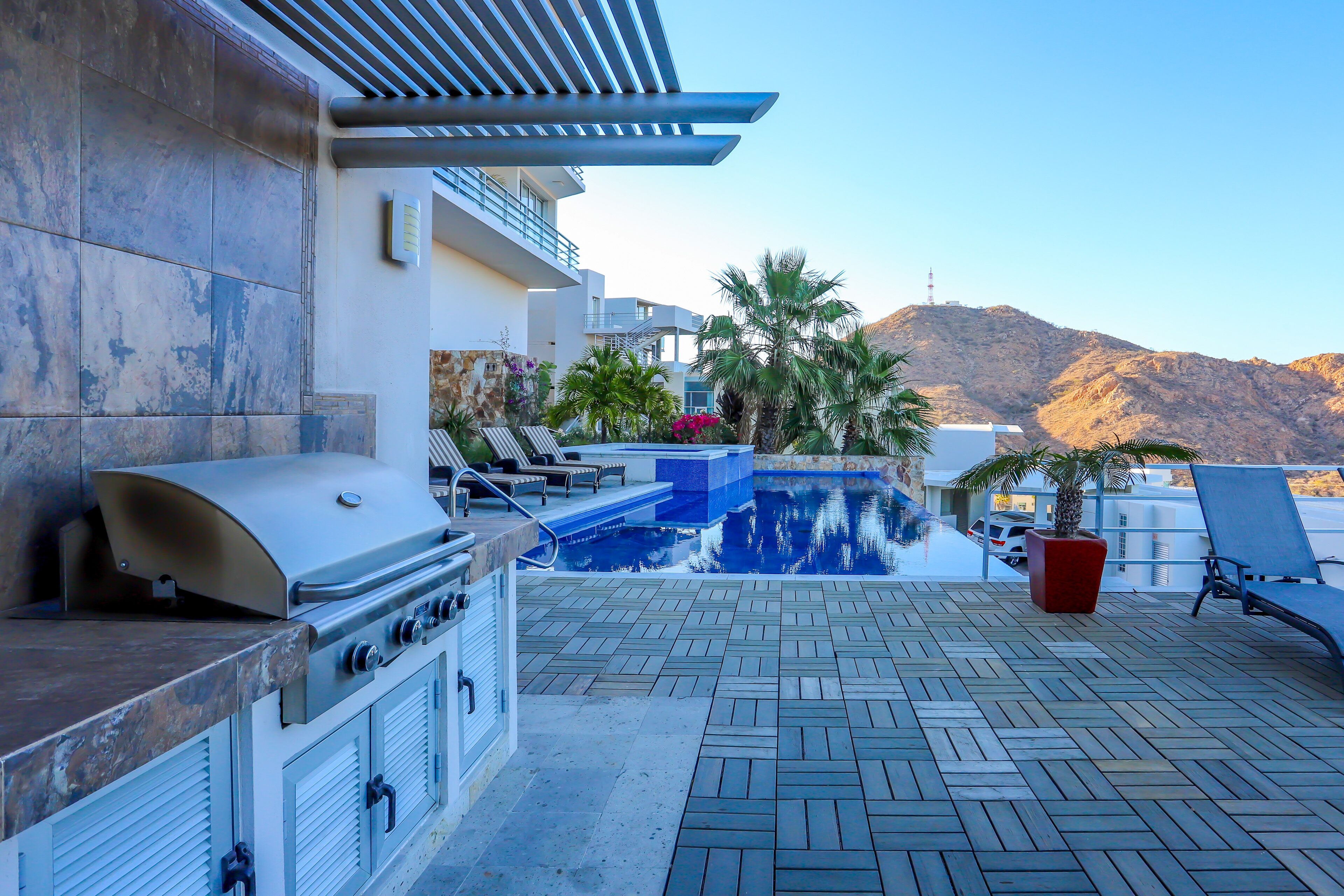 Un patio exterior con una parrilla, sillones de descanso, una piscina y vistas a la montaña.