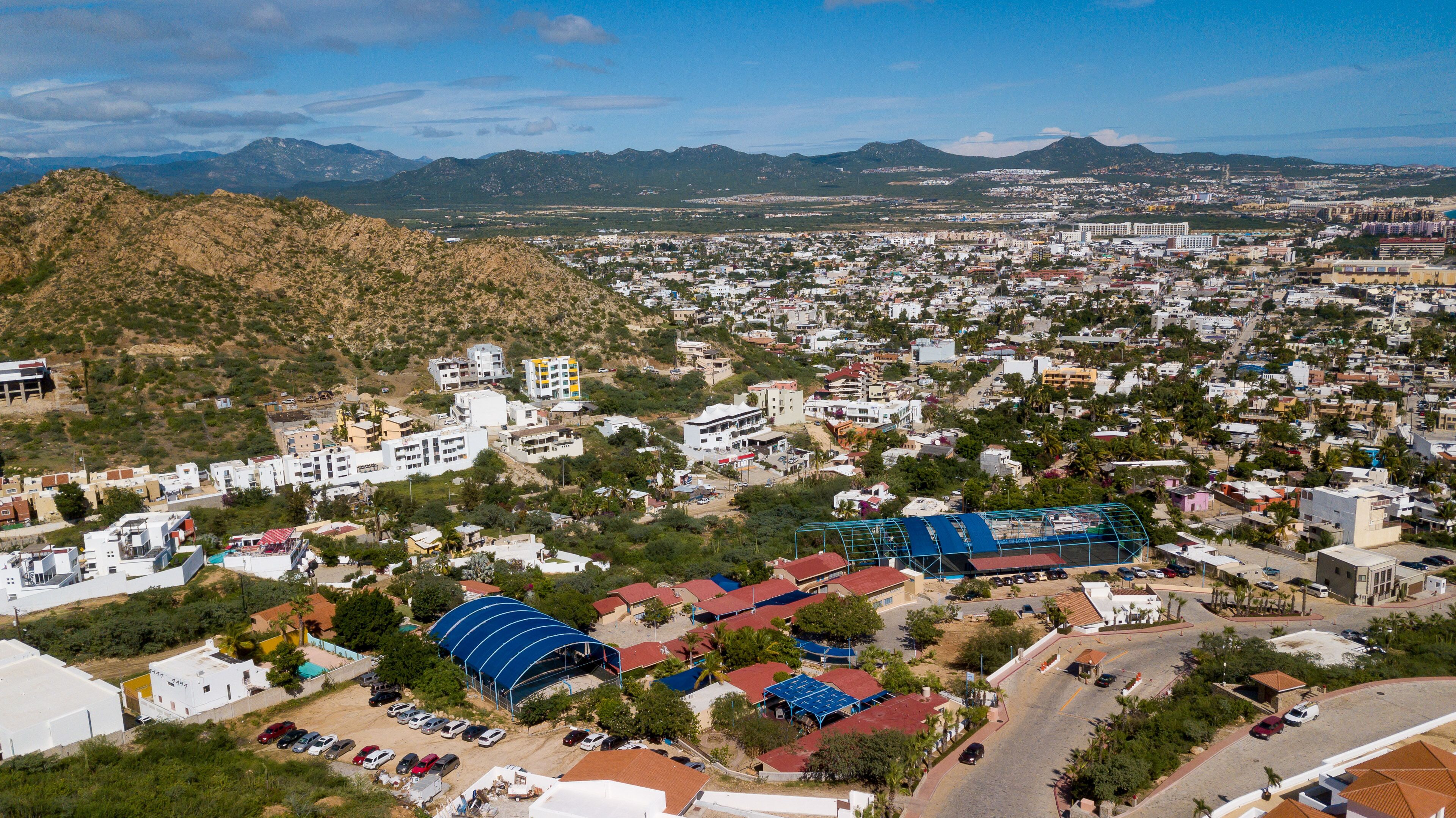 Un paysage urbain composé d’un mélange de bâtiments résidentiels et commerciaux, avec une structure remarquable surmontée d’un toit bleu, et un paysage montagneux en arrière-plan.