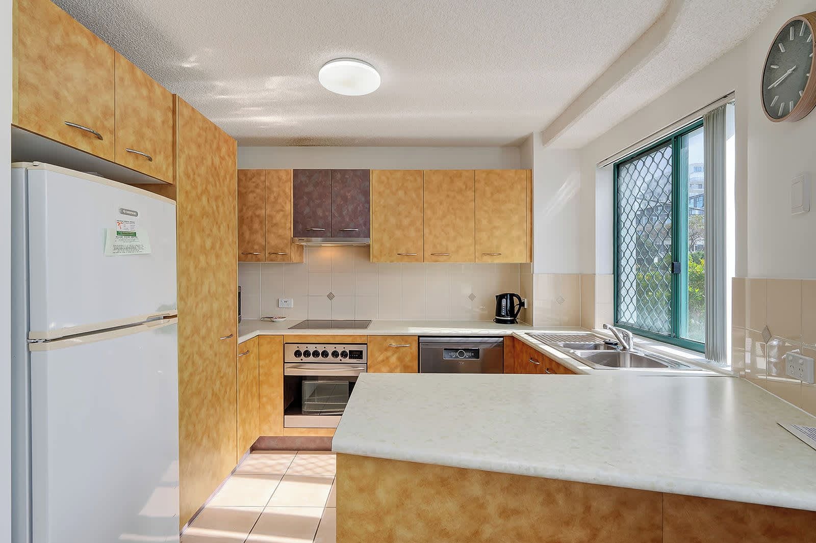Una cocina compacta con armarios de madera, horno empotrado, lavavajillas y ventana con vistas.