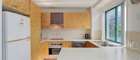 Una cocina compacta con armarios de madera, horno empotrado, lavavajillas y ventana con vistas.