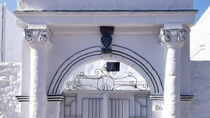 A white building with a large arched entrance, flanked by columns, and a decorative metal gate with the number 86. - Traditional Villa Sofia - a Greek village dream!! (Koskinou)