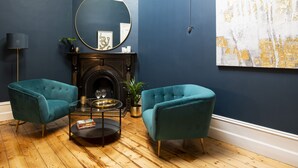 A room with dark blue walls, a fireplace, two teal armchairs, a round mirror, and a large abstract painting. - Charming Historic Home With Modern Interior - In The Heart Of Ballarat (Ballarat Central)
