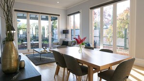 A spacious living area with a large dining table, comfortable seating, and large windows offering views of the outdoors. - Charming Historic Home With Modern Interior - In The Heart Of Ballarat (Ballarat Central)