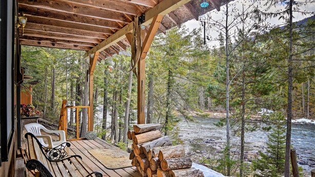 Une terrasse en bois avec des bancs, donnant sur une rivière et entourée d’arbres.