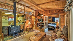 Un intérieur de chalet chaleureux avec une cheminée, des meubles en bois et une chambre à coucher située en mezzanine.