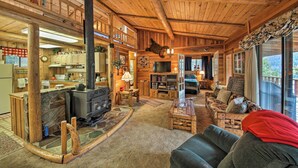L’intérieur chaleureux d’un chalet avec une cheminée en pierre, des meubles en bois et une grande fenêtre donnant sur un paysage magnifique.