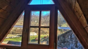 A triangular window with a view of a grassy area and a stone wall.
