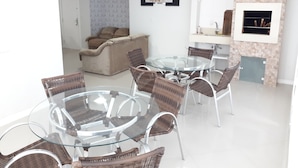 Un salon moderne avec une table à manger en verre, entourée de chaises en osier, d’un canapé et d’une cheminée.