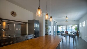Una cucina moderna con elettrodomestici in acciaio inossidabile, un'isola in legno, illuminazione a sospensione e vista sull'area pranzo con tavolo e sedie.