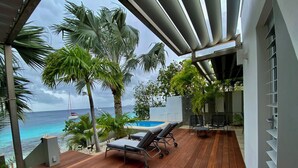 Un terrazzo in legno con poltrone relax e una piccola piscina, con vista sull'oceano e imbarcazioni all'orizzonte.