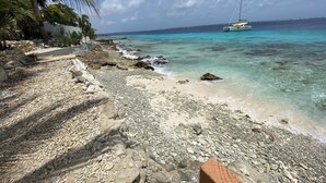 Una spiaggia con acque turchesi cristalline, una barca a vela e un litorale roccioso con delle scale che conducono all'acqua.