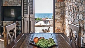 Une pièce avec un mur en pierre, une table en bois sur laquelle sont disposés des fruits, un téléviseur et une vue sur la mer.
