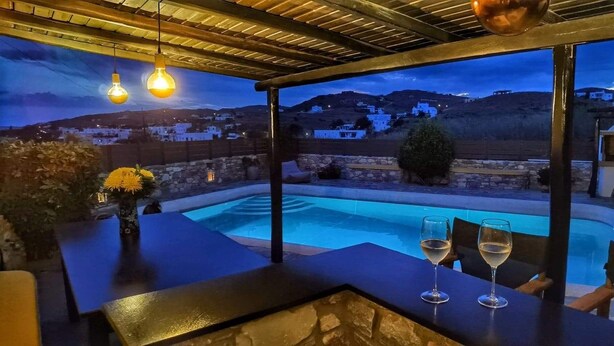 Un espace aménagé au bord de la piscine, offrant une vue sur un village et des montagnes au crépuscule.