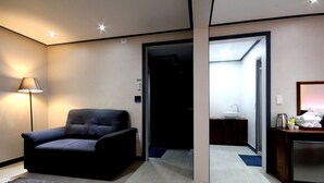 A modern hotel room with a dark-colored sofa, a bedside table with a lamp, and a small kitchenette area. - Hotel Luna (Jeonju)