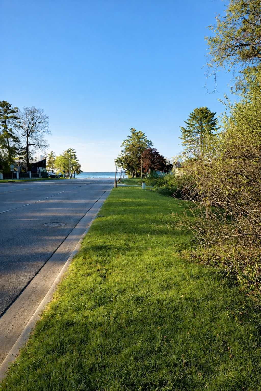 A well-maintained grassy area beside a road with a clear view of the ocean in the distance.