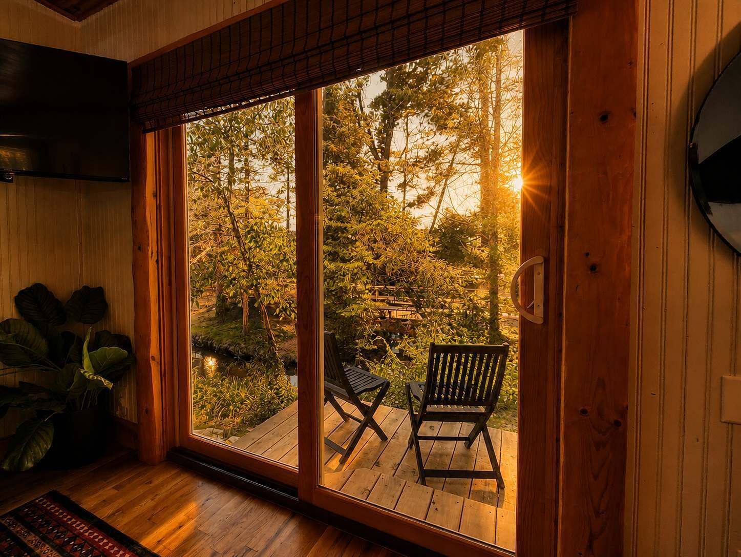 A room with a sliding glass door leading to an outdoor deck with two chairs and a view of trees.