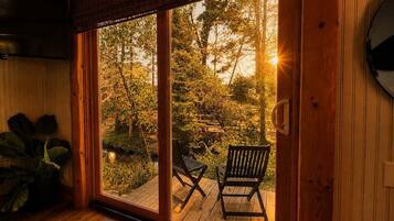 A room with a sliding glass door leading to an outdoor deck with two chairs and a view of trees.