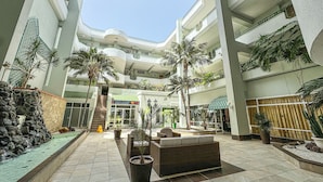 Een meerlaags atrium met een centrale trap, palmbomen en een Costa Caleta restaurant.