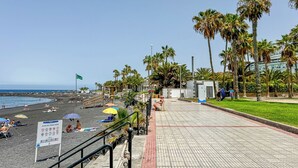Een promenade aan het strand met palmbomen, een zandstrand en een bord waarop de strandregels staan.