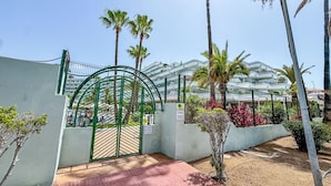 Een poort met een groene boogpartij, palmbomen en een gebouw met een modern ontwerp op de achtergrond.