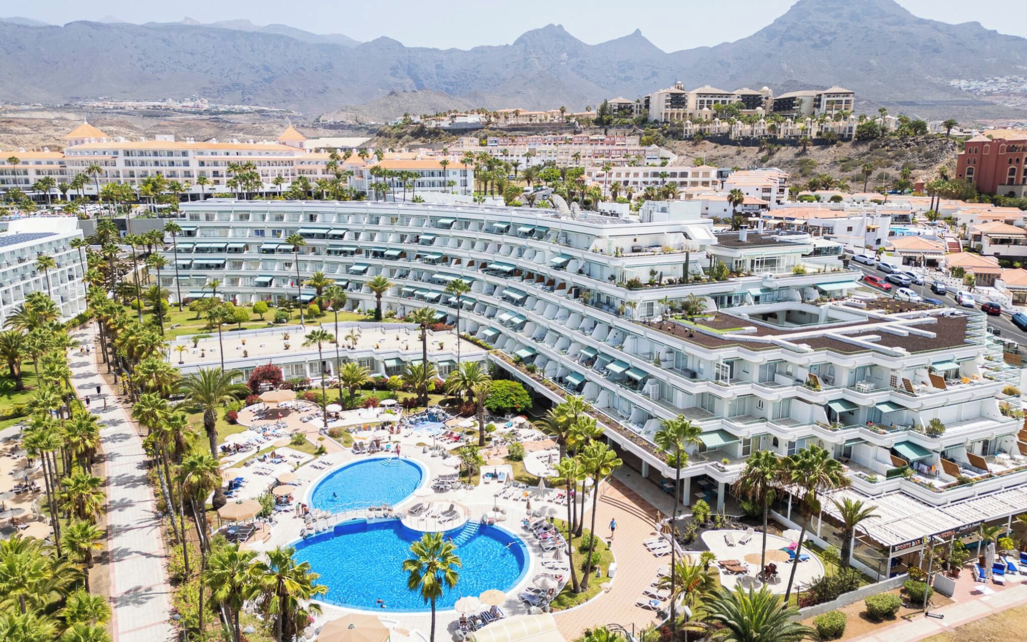 Ein Resort mit mehreren Schwimmbecken, einem zentralen Innenhof und Blick auf die umliegenden Berge.